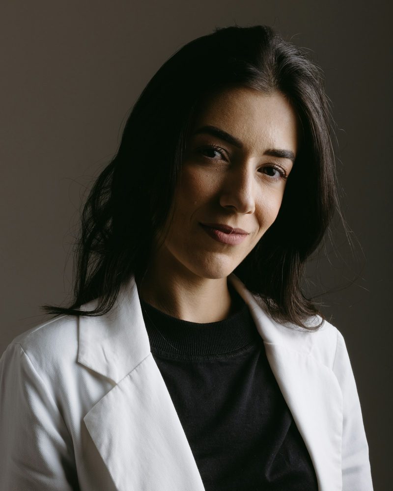 Portrait von Dr. Anna Berger, Zahnärztin, mit langen dunklen Haaren und weißem Kittel